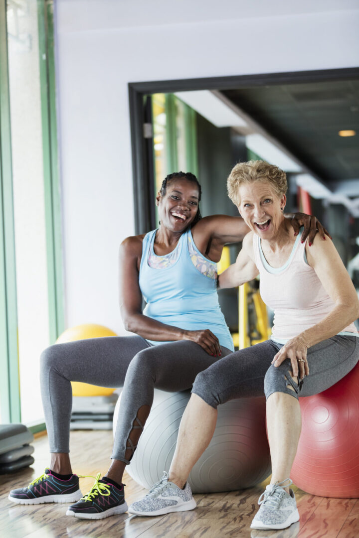 Two women sitting on a red ball in the gym